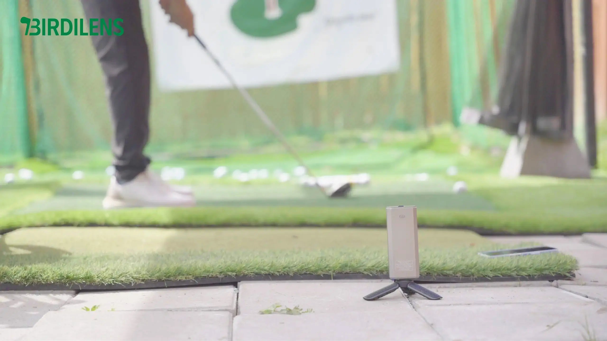 A golfer addresses the ball and prepares to swing, with a launch monitor set up nearby to capture the shot data.