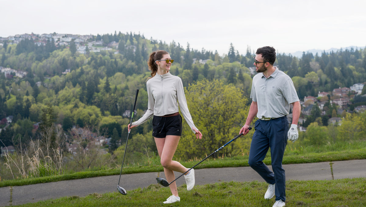 Two people walking with golf clubs on a path surrounded by greenery