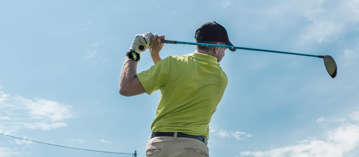 Man in a yellow shirt and black cap playing golf against a blue sky.